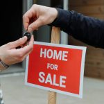 Overdracht van huissleutels bij &ldquo;Home For Sale&rdquo;-bord, passend bij verkoopproces met makelaar in Roosendaal.