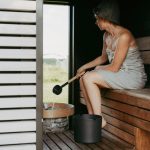 Vrouw ontspant in een moderne sauna in huis en giet water op de hete stenen voor extra warmte