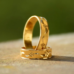 Set van twee klassieke gouden trouwringen met gravure en bloemmotief, staand op een houten oppervlak