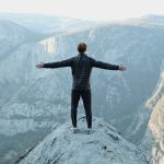 Persoon staat op bergtop met frisse buitenlucht als symbool voor optimale luchtkwaliteit werkplek en energie